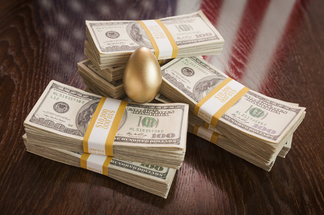 Golden Egg and Thousands of Dollars with American Flag Reflection on Table.