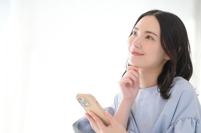スマホを片手に考え事をするビジネスパーソン