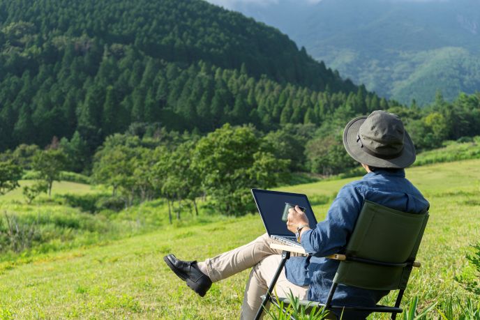 地方在住の男性が自然の中でノートパソコンを使いハイブリッドワークを行い、ワークライフバランスを実現している様子