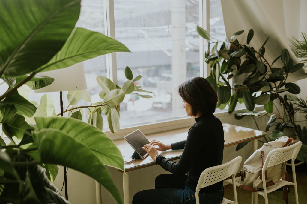 自然光と緑を取り入れた快適なオフィス空間で、窓際のデスクにて作業を行うビジネスパーソン