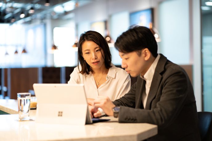 サーブコープYanmar Tokyoのコワーキングラウンジで、AI活用を加速させるためにバイリンガル秘書と個人事業主が打ち合わせをしている様子