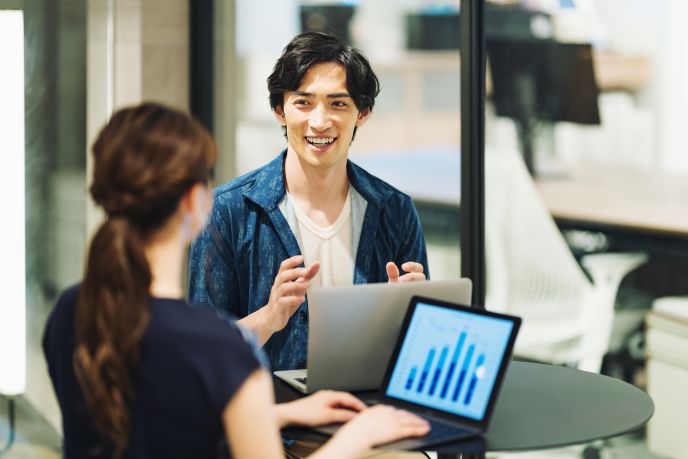 モダンなオフィス環境で、ノートパソコンを使って打ち合わせを行うビジネスパーソン