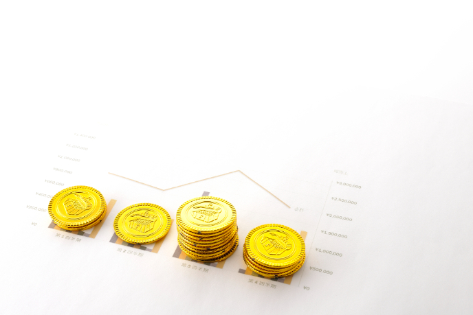 積み上がった金色のコインと売上推移グラフで年商を表したイメージ