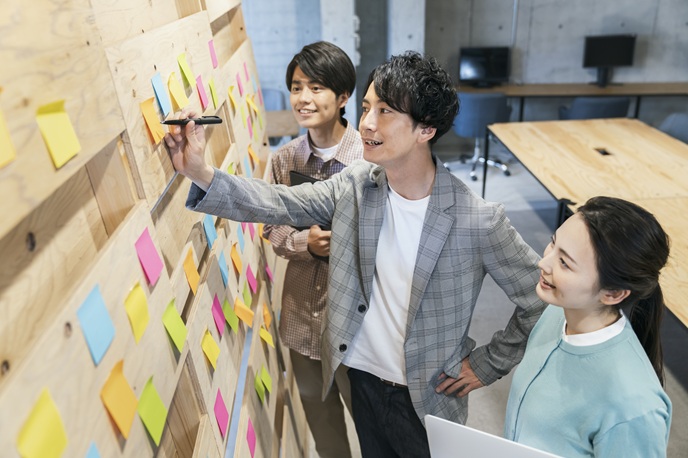 アイデアを出し合い付箋にメモする3人のビジネスパーソン
